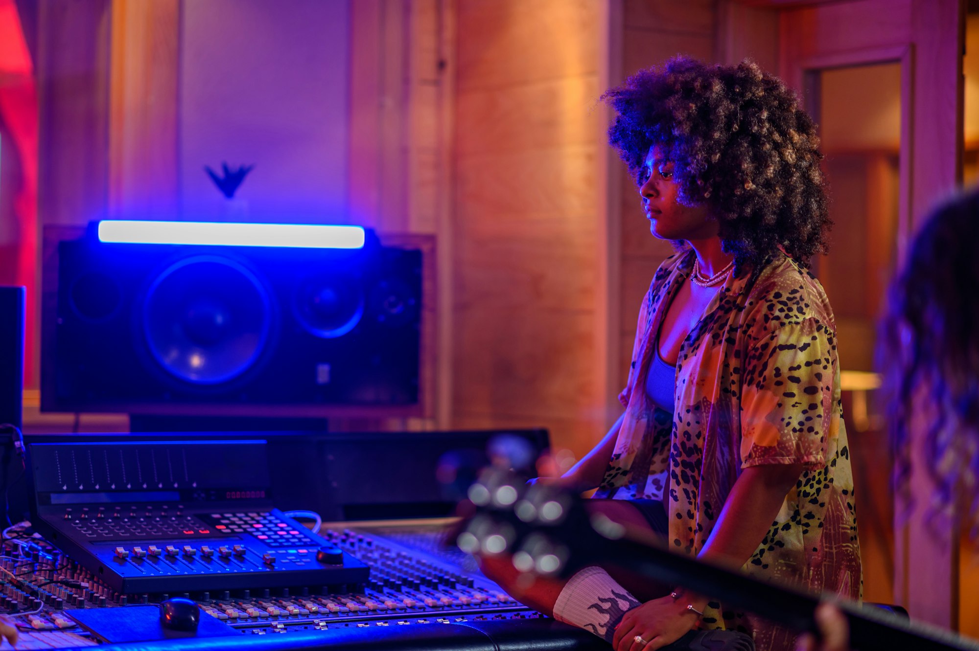 A musician standing next to a mixing console in a studio with a guitar player