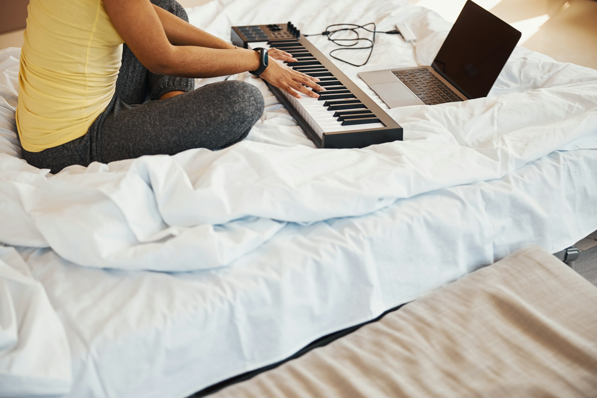 Female musician playing synth and using notebook at home