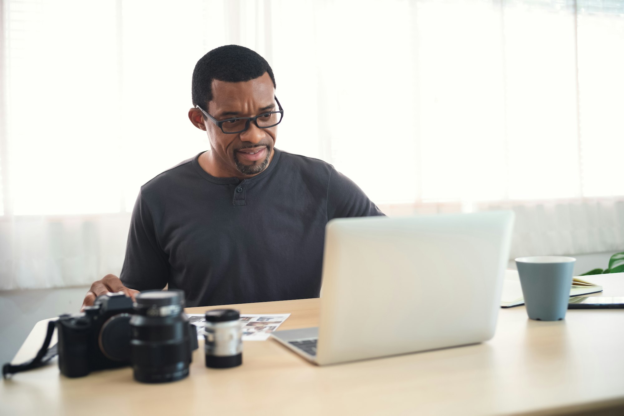 Portrait of handsome african photographer off loading files on laptop computer at his workplace.