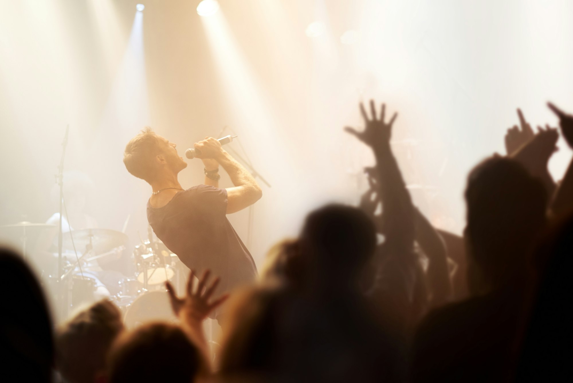 Rocking out. A rock star singing into his mic while fan reach out their hands to him.