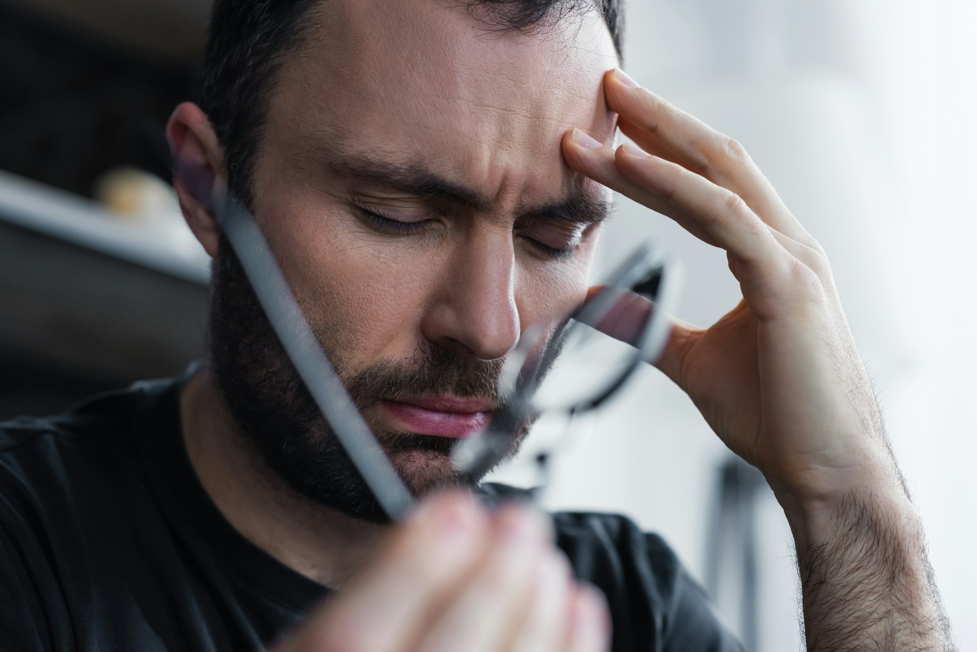 selective focus of frustrated man with closed eyes holding hand near head