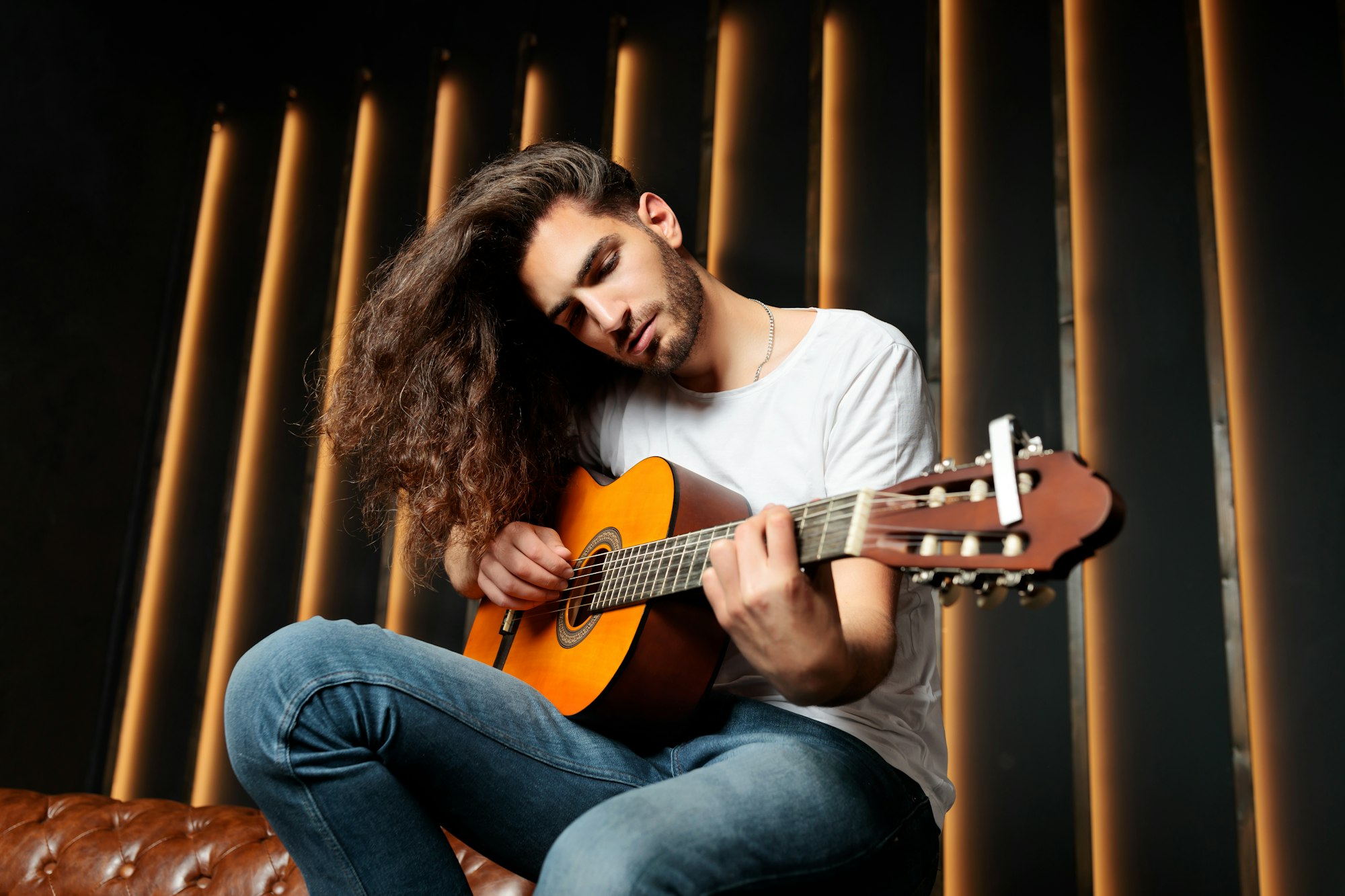 Talented Latin Guy Playing Guitar Sitting In Dark Black Studio