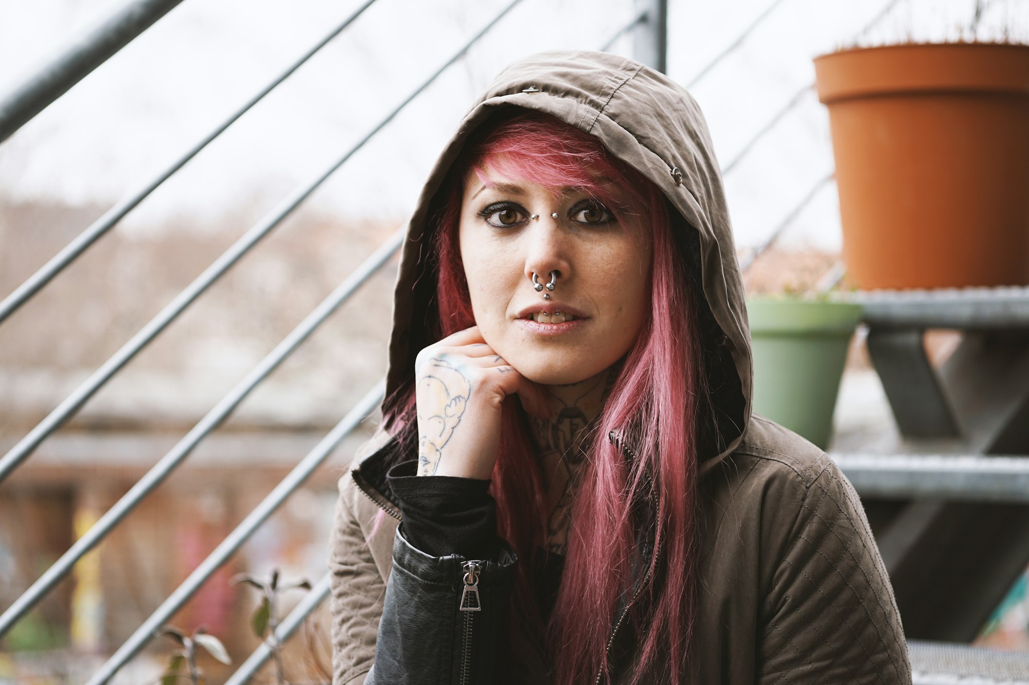 thoughtful young woman with piercings and tattoos sitting on outside staircase