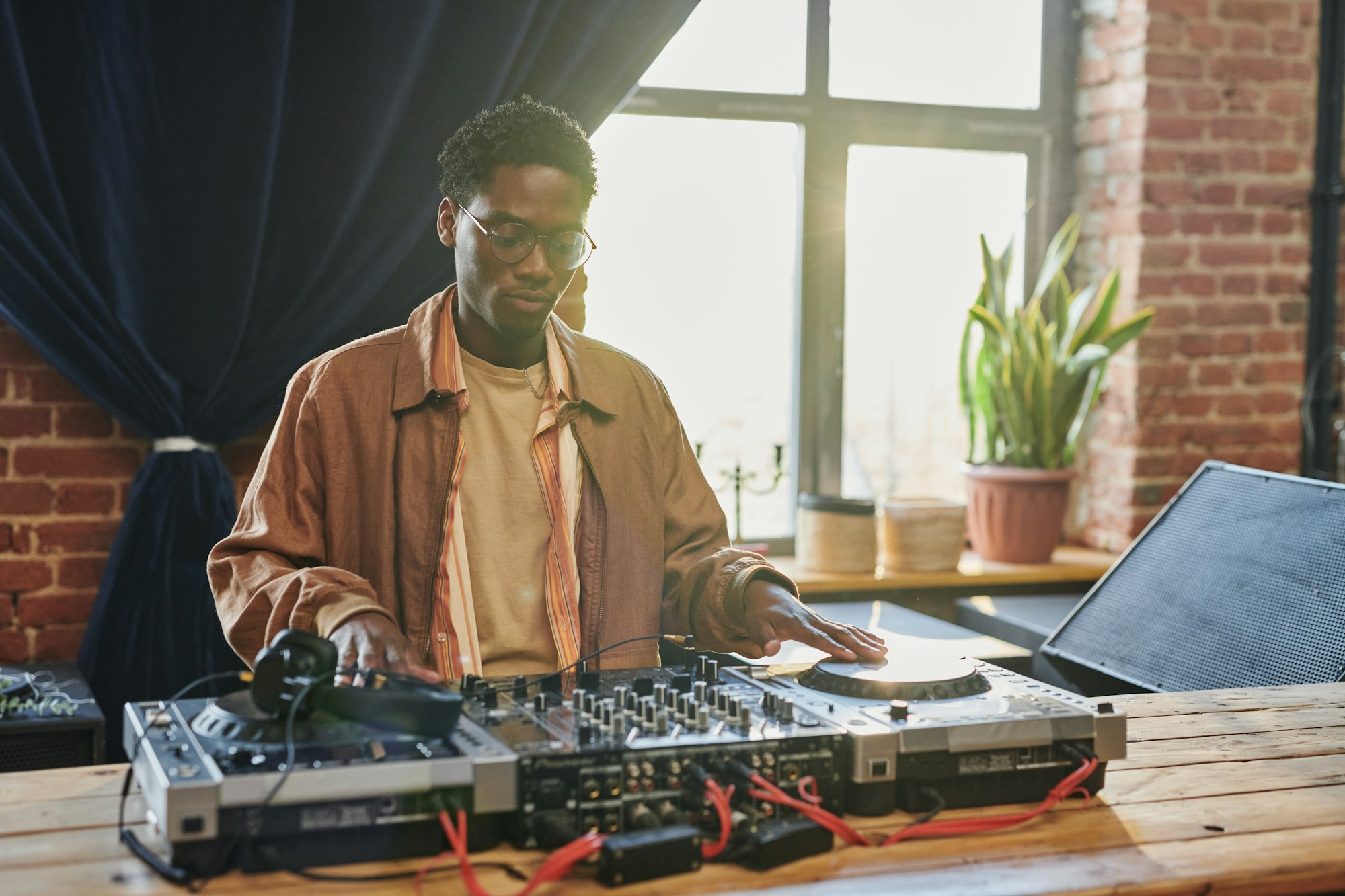 Young serious black man looking at dj board while touching turntables